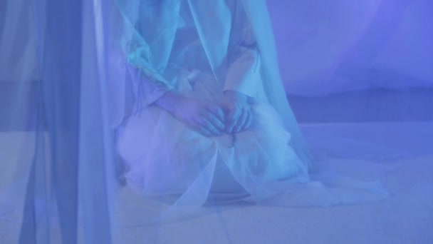 Μια νεαρή γυναίκα με άσπρα κάνει μια προσευχή πίσω από μια λευκή κουρτίνα. — Αρχείο Βίντεο