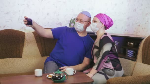 Εβραϊκό παντρεμένο ζευγάρι με προστατευτικές μάσκες σε καραντίνα για την πρόληψη του coronavirus στο σπίτι στον καναπέ φωτογραφίζονται με μάσκες — Αρχείο Βίντεο