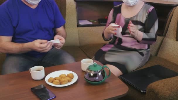 Een echtpaar met beschermende maskers in quarantaine voor de preventie van coronavirus thuis op de bank desinfecteert hun handen en smartphones met servetten. — Stockvideo