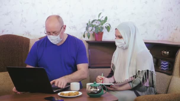 穆斯林夫妇戴着防护面罩，在家中进行隔离，以防止考拉韦在沙发上从事远程工作 — 图库视频影像