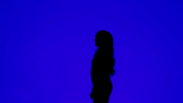 Silhouette of a young woman with curly hair talking on a cell phone on a blue background — ストック動画