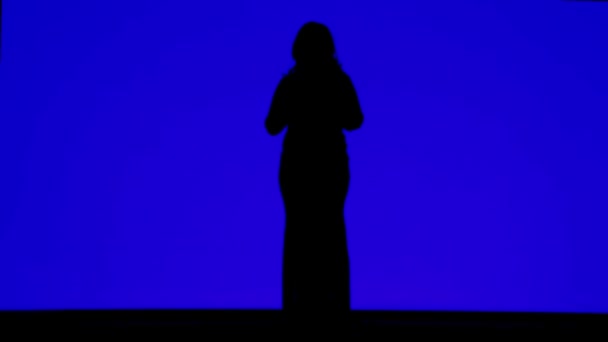 Silhouette d'une femme élancée en casque dansant sur fond bleu — Video