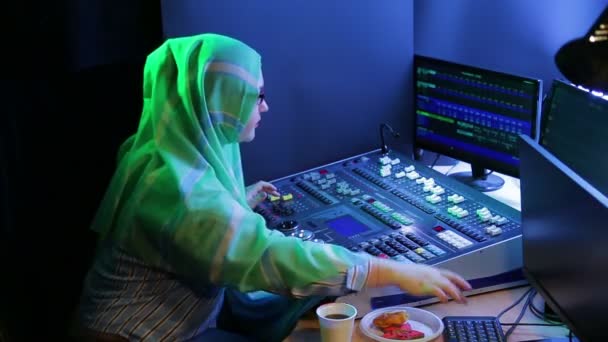 Femme musulmane dans un foulard et des lunettes, un concepteur d'éclairage programme la lumière, boit du café et mange de la restauration rapide — Video