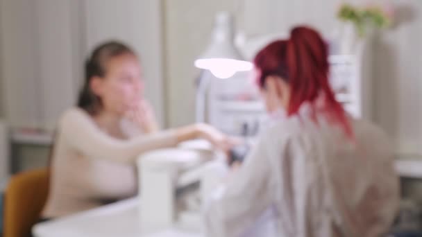 Güzellik salonunda eldivenli kadın manikürcü jel kaplama uygulamadan önce müşteriye manikür yapıyor. Görüntü odak dışı — Stok video