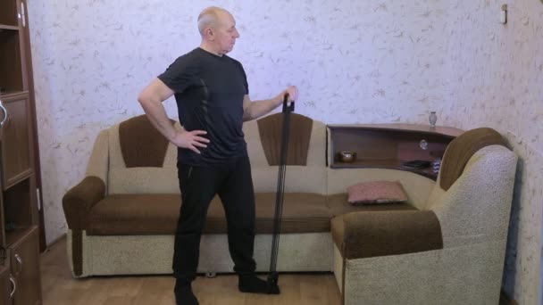 En man i ett vardagsrum i träning gör stretching övningar med en expander — Stockvideo