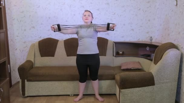 Молодая женщина в гостиной на тренировке делает упражнения на растяжку с расширителем — стоковое видео