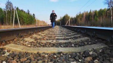 Koruyucu tıbbi maskeli bir kadın tren yolu boyunca elinde bavulla yürüyor..