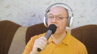 Evde kulaklıklı bir adam karaoke mikrofonunda şarkı söylüyor.