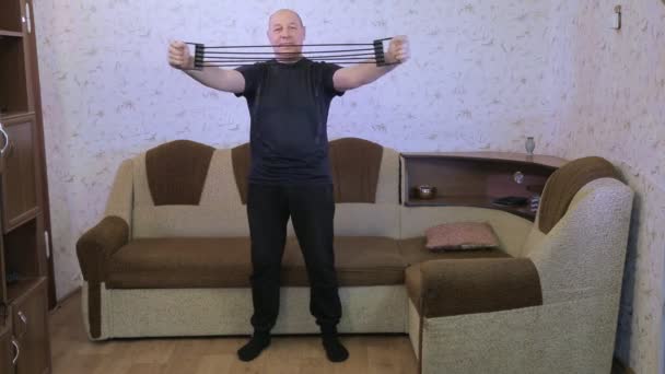 En man i ett vardagsrum i träning gör stretching övningar med en expande — Stockvideo