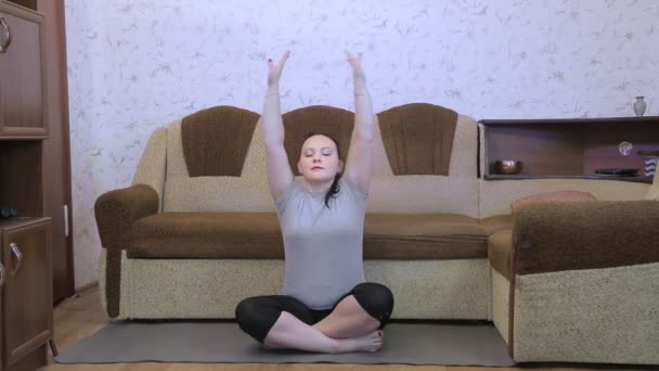 Egy fiatal nő a nappaliban a lábtörlőn jógázik, légzési gyakorlatokat végez. — Stock videók
