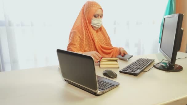 Mulher muçulmana em hijab em uma máscara médica durante o período de quarentena trabalha no escritório com informações — Vídeo de Stock