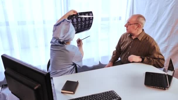 Μια γυναίκα γιατρός καθιερώνει μια διάγνωση για έναν άνδρα σύμφωνα με τα αποτελέσματα της απεικόνισης μαγνητικού συντονισμού του εγκεφάλου. — Αρχείο Βίντεο