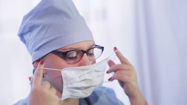 Egy női orvos a munka megkezdése előtt orvosi maszkot vesz fel. — Stock videók