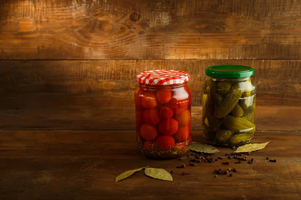 Burkar med saltade pickles och körsbärstomater på ett träbord. — Stockfoto