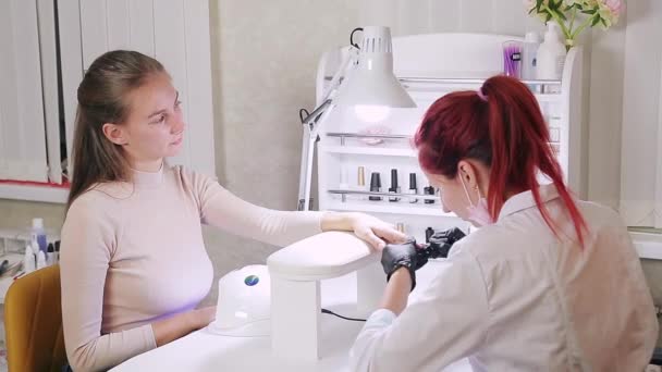 Vrouw manicure in een schoonheidssalon brengt violette gel polish aan op de nagels van een klant. Het meisje droogt haar nagels in een speciale lamp — Stockvideo