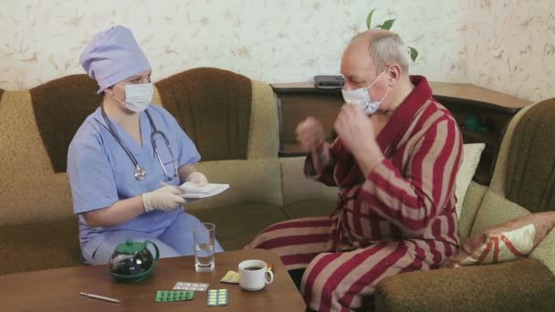 Uma médica do sexo feminino instrui um paciente do hospital em casa para tomar remédio. Um homem bebe comprimidos . — Vídeo de Stock