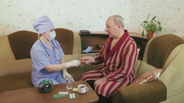 Нездоровый человек в халате измеряет температуру под наблюдением врача дома — стоковое видео