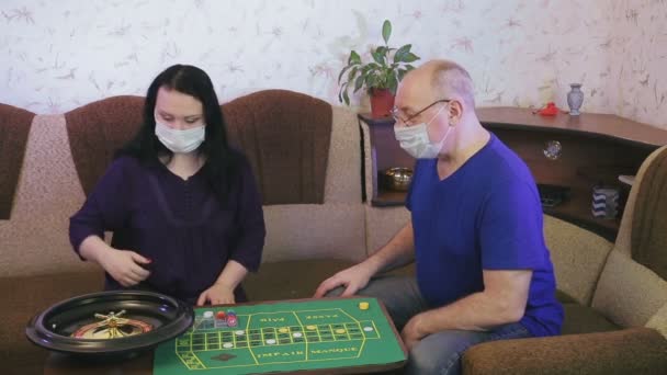 Una coppia sposata in maschere mediche gioca alla roulette a casa in quarantena per la prevenzione del coronavirus . — Video Stock