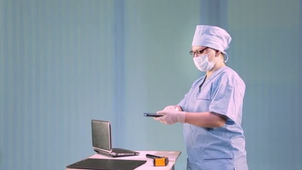 Uma médica em uma máscara médica mostra como desinfetar um local de trabalho — Vídeo de Stock