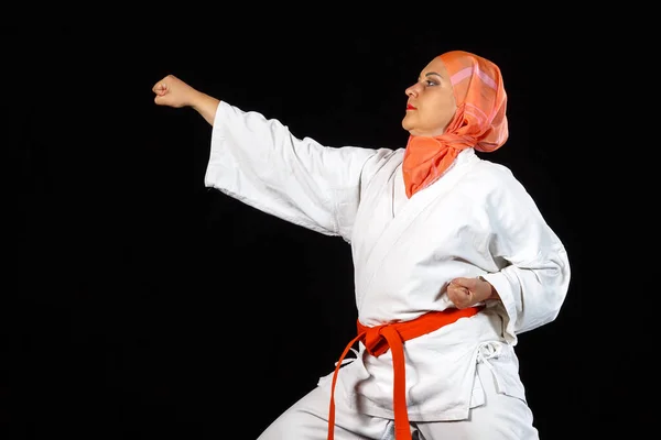 Ung muslimsk kvinna i kimono och sjal under karate träning över svart bakgrund. — Stockfoto