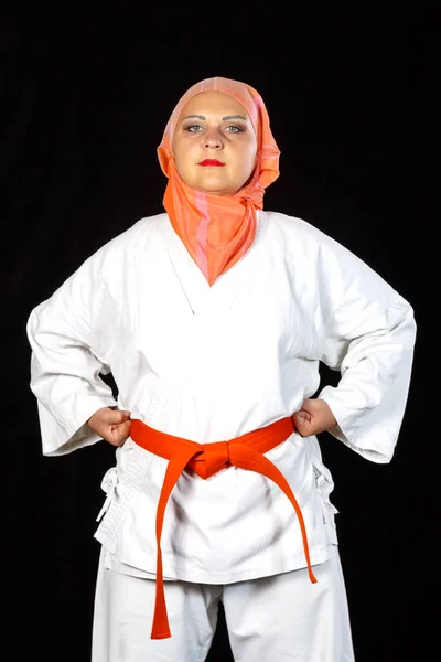 Junge Muslimin im Kimono und Hijab im Karatetraining vor schwarzem Hintergrund. Nahaufnahme. — Stockfoto