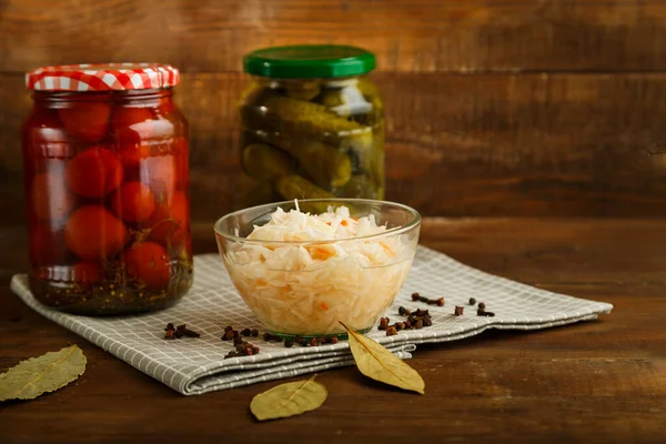 Gläser mit eingelegten Tomaten und Gurken mit hausgemachten Essiggurken und Sauerkraut auf einem Holztisch. — Stockfoto
