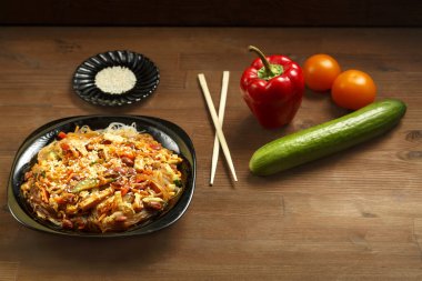 Funselli siyah tabak, sebzeli tavuk ahşap bir masada Tayland sosu ve taze sebzeler..