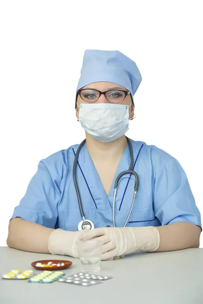 Женщина-врач сидит за столом в медицинской маске рядом с таблеткой . — стоковое фото