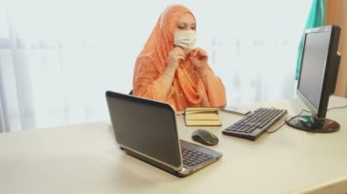 Karantina döneminde tıbbi maske takmış Müslüman bir kadın ofiste aletlerle çalışıyor..