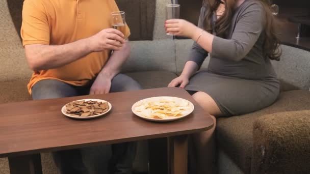 Een man en een vrouw op de bank drinken bier en kijken tv zonder gezichten — Stockvideo