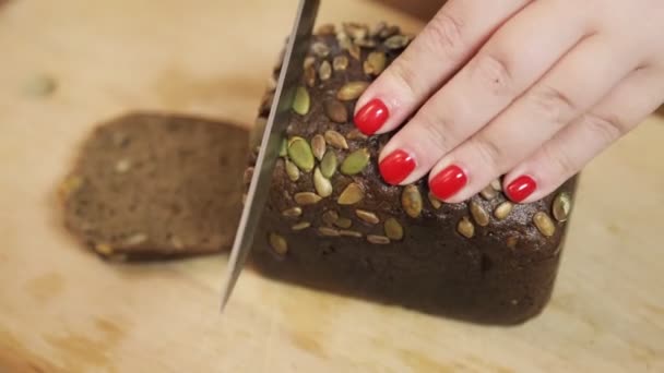 Female hand cuts a large knife on a wooden board rye hlnb with bran — Stock Video