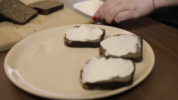 Una mano femminile stende il pane di segale scuro con la crema di formaggio usando un coltello — Video Stock