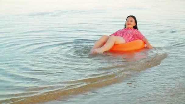 A brunette woman dangles in a swimming circle in the sea near the shore — Stock Video