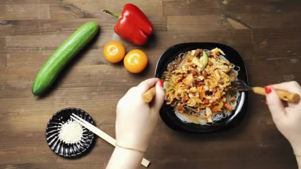 A female hand puts in a plate with funchose stewed vegetables with chicken a ready-made dish of funchose with chicken and vegetables — Stock Video