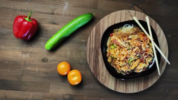 Фунчоза з куркою та овочами на чорній тарілці обертається в колі — стокове відео