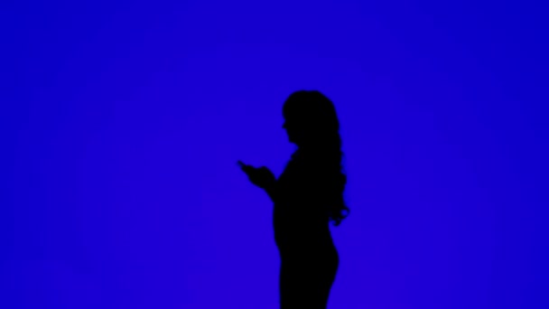 Silhouette einer Frau mit lockigem Haar, die in einem Boten auf einem Tablet auf blauem Hintergrund kommuniziert — Stockvideo