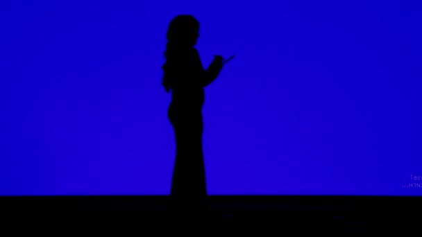 Silhouette di una donna snella con i capelli ricci che schizzano in un notebook su uno sfondo blu — Video Stock