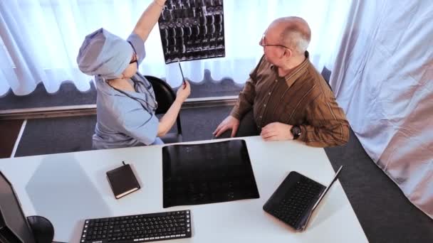Žena lékař řekne muži diagnózu na základě výsledků magnetické rezonance zobrazování páteře. — Stock video