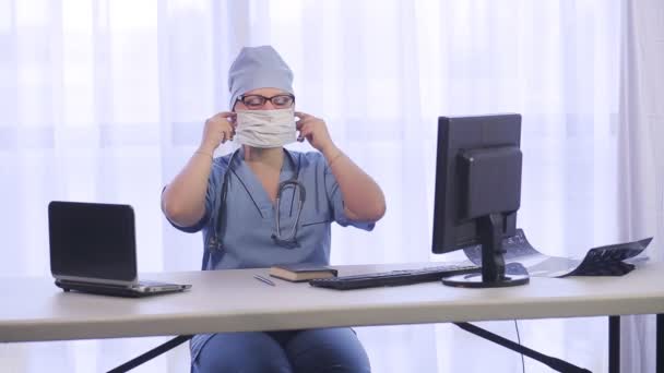 Bir kadın doktor, işe başlamadan önce, ofise tıbbi maske takar. — Stok video