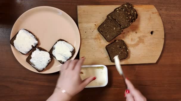 Een vrouwelijke hand spreidt roggebrood uit met roomkaas met een mes — Stockvideo