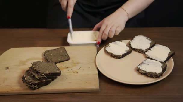 一只雌性的手在黑麦面包上撒满了麸皮奶油奶酪和一把刀 — 图库视频影像