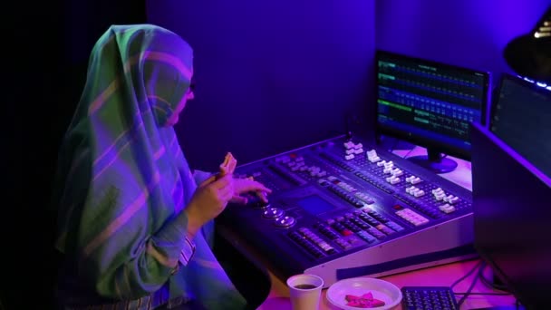Mulher muçulmana em um lenço de cabeça e óculos, um designer de iluminação bebe café e come fast food . — Vídeo de Stock