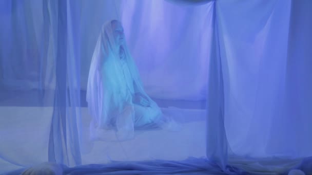 Una joven musulmana de blanco hace una oración antes de la boda detrás de una cortina blanca . — Vídeos de Stock