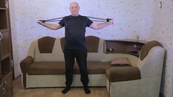 Een man in een woonkamer in opleiding doet stretching oefeningen met een expander. — Stockvideo
