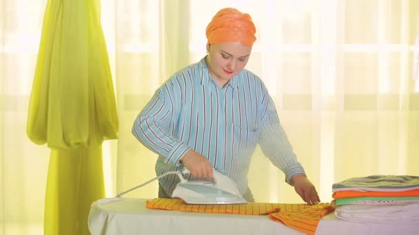 Еврейская домохозяйка гладит цветную одежду на гладильной доске дома — стоковое видео