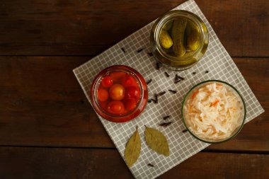 Salatalık turşulu kavanozlar, domatesler, lahana turşusu, ahşap bir masa, siyah bir arka plan ve keten bir havlu..