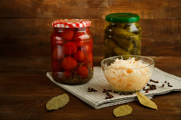 Gläser mit eingelegten Tomaten und Gurken mit hausgemachten Essiggurken und Sauerkraut auf einem Holztisch. — Stockfoto