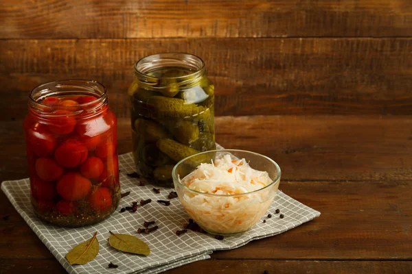 Burkar med inlagda tomater och gurkor och surkål på ett träbord. — Stockfoto