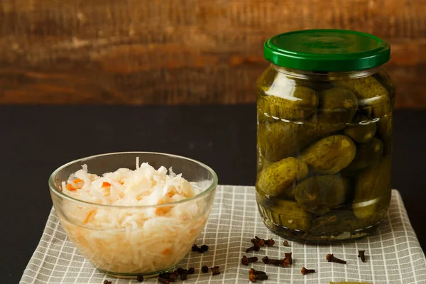 Frascos con pepinos en escabeche y chucrut sobre una mesa de madera sobre un fondo negro . —  Fotos de Stock