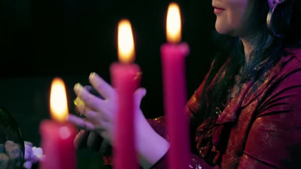 A fortuneteller in a mashine salon works with cards through candles on a black background. — Stock Video